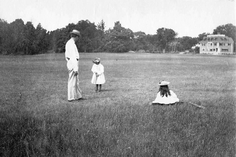 Black and white photo of 2 children playing croquet with an adult