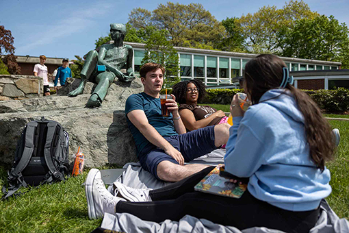 Students sit outside on the Brandeis campus on a sunny summer day.