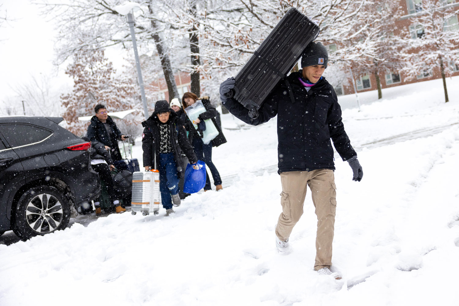 Student carrying a suitcase over his shoulder through the snow
