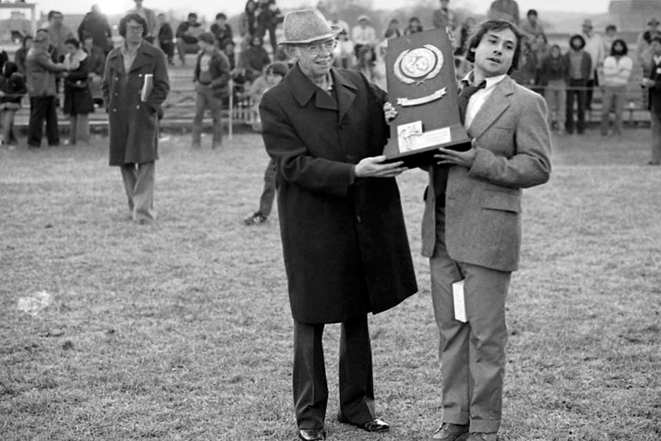 Black and white photo of Mike Coven accepting a trophy