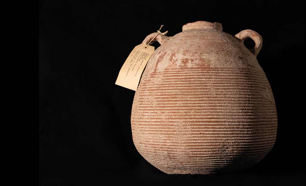 A brown jar, round in shape, with two small handles on either side near the small mouth