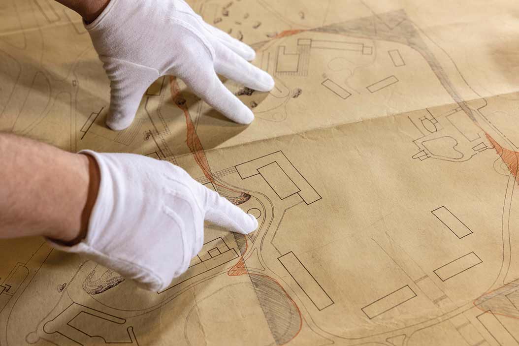 White-gloved hands point to an area on a schematic drawing.