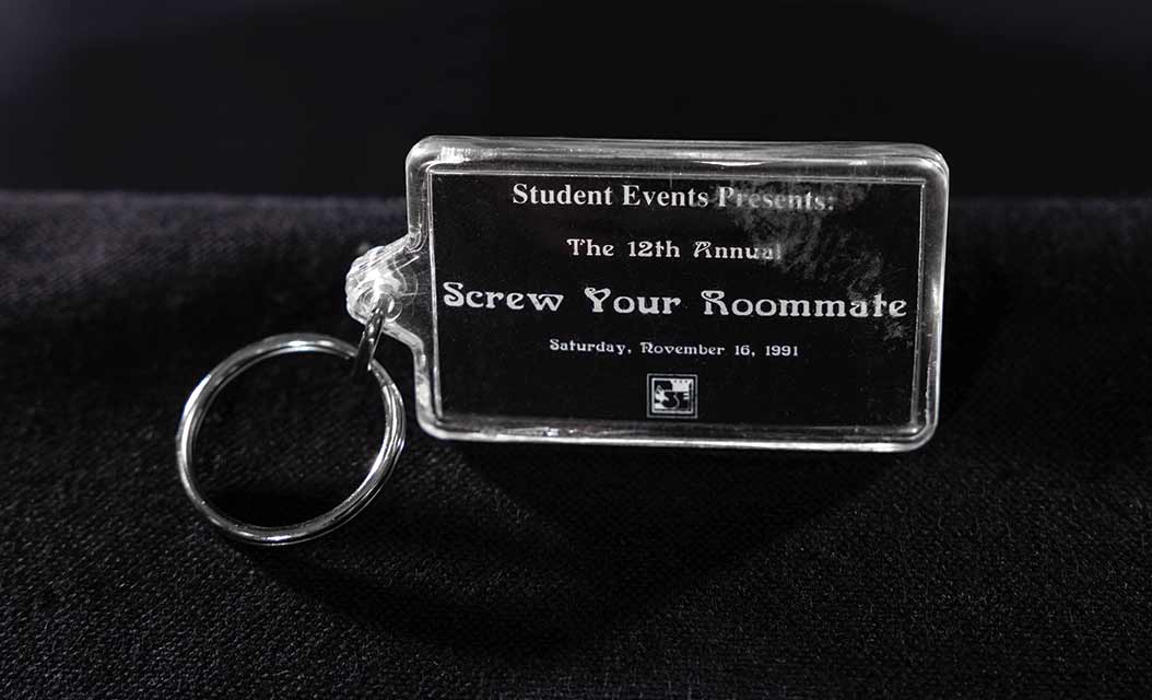 A photo of a clear plastic keychain labeled "Student Events Presents / The 12th Annual / Screw Your Roommate / November 16, 1991."