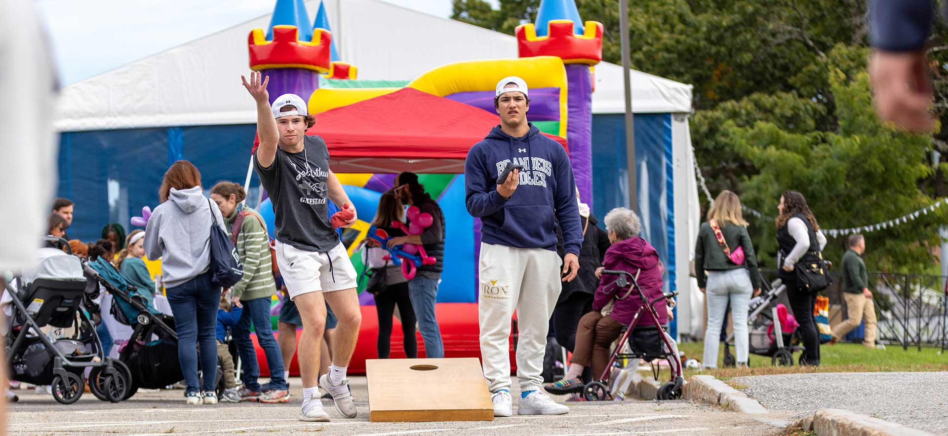 Two students playing cornhole with a bouncy house in the background