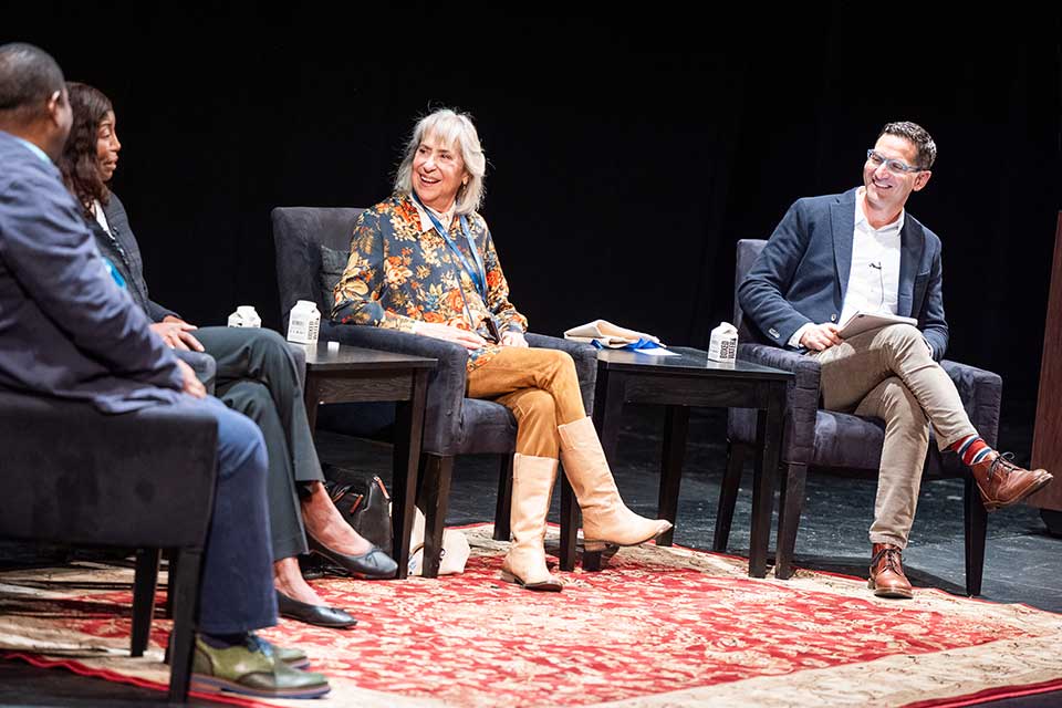 Guy Raz and Letty Cottin Pogrebin laugh sitting on stage during the session