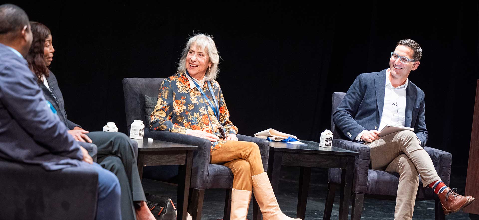 Guy Raz and Letty Cottin Pogrebin laugh sitting on stage during the session