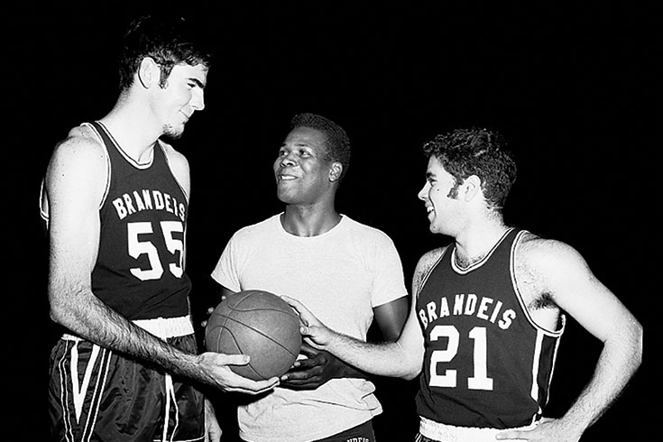 K.C. Jones stands between two basketball players, holding a basketball