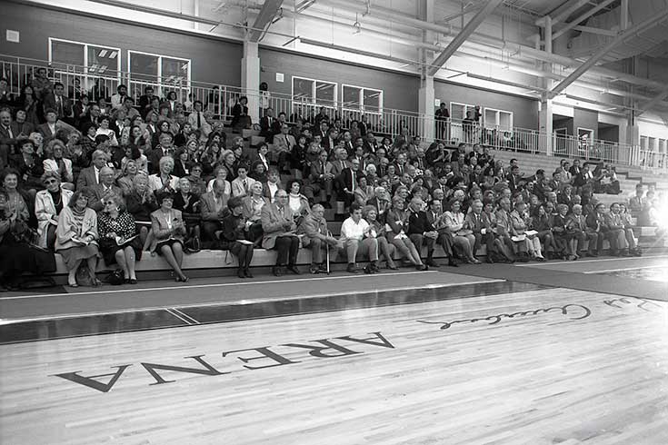 Black and white photo of people sitting in the bleachers at a basketball court