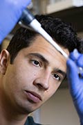 A student researcher wearing goggles pours a clear liquid into a test tube