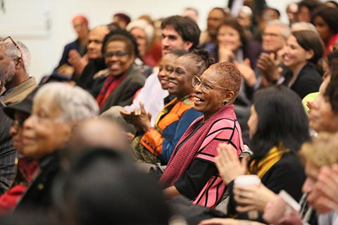 Hortense Spillers sits in the audience with big smile; others around her clap.