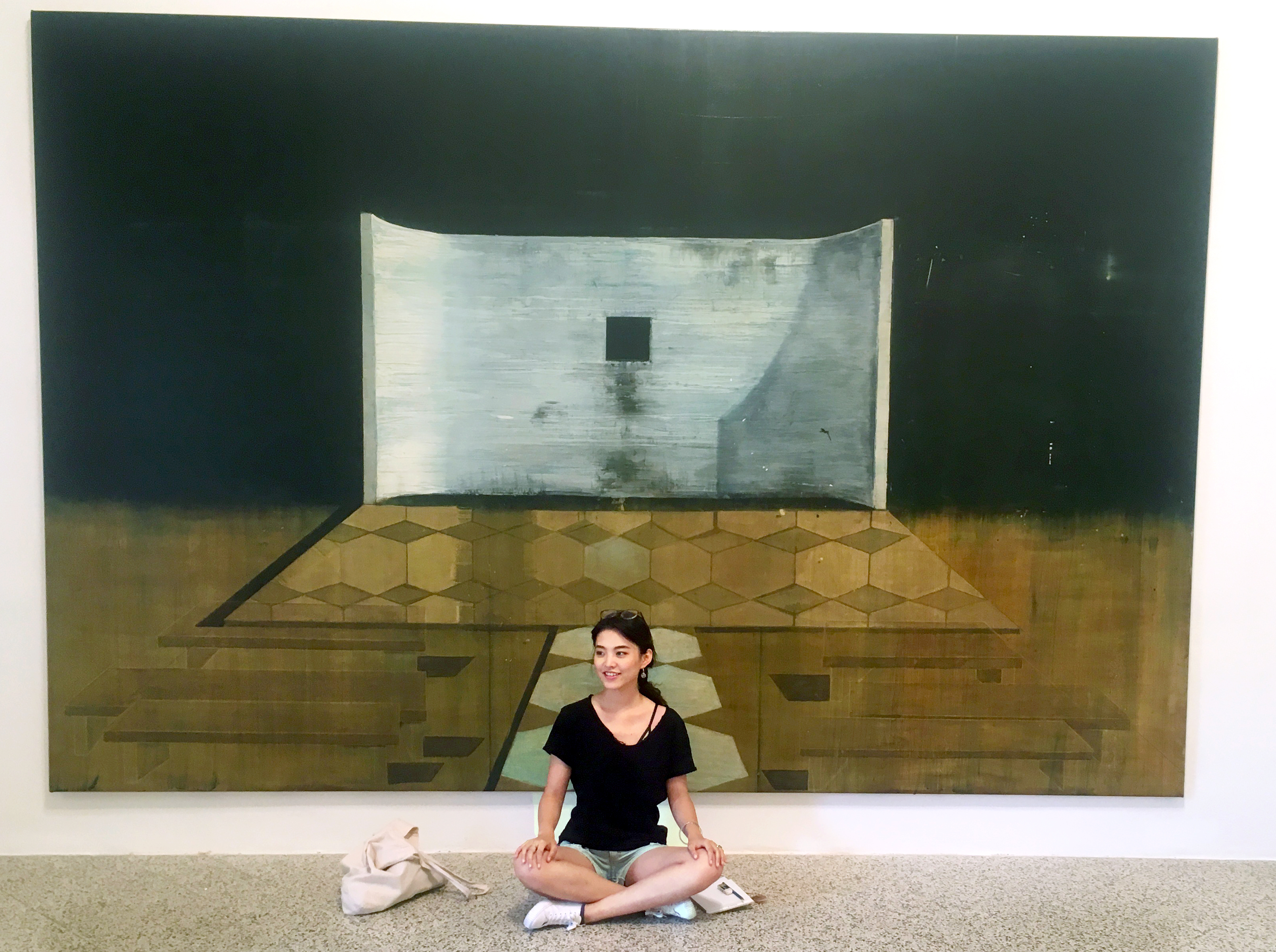 Carrie sitting cross-legged in front of a piece of art.