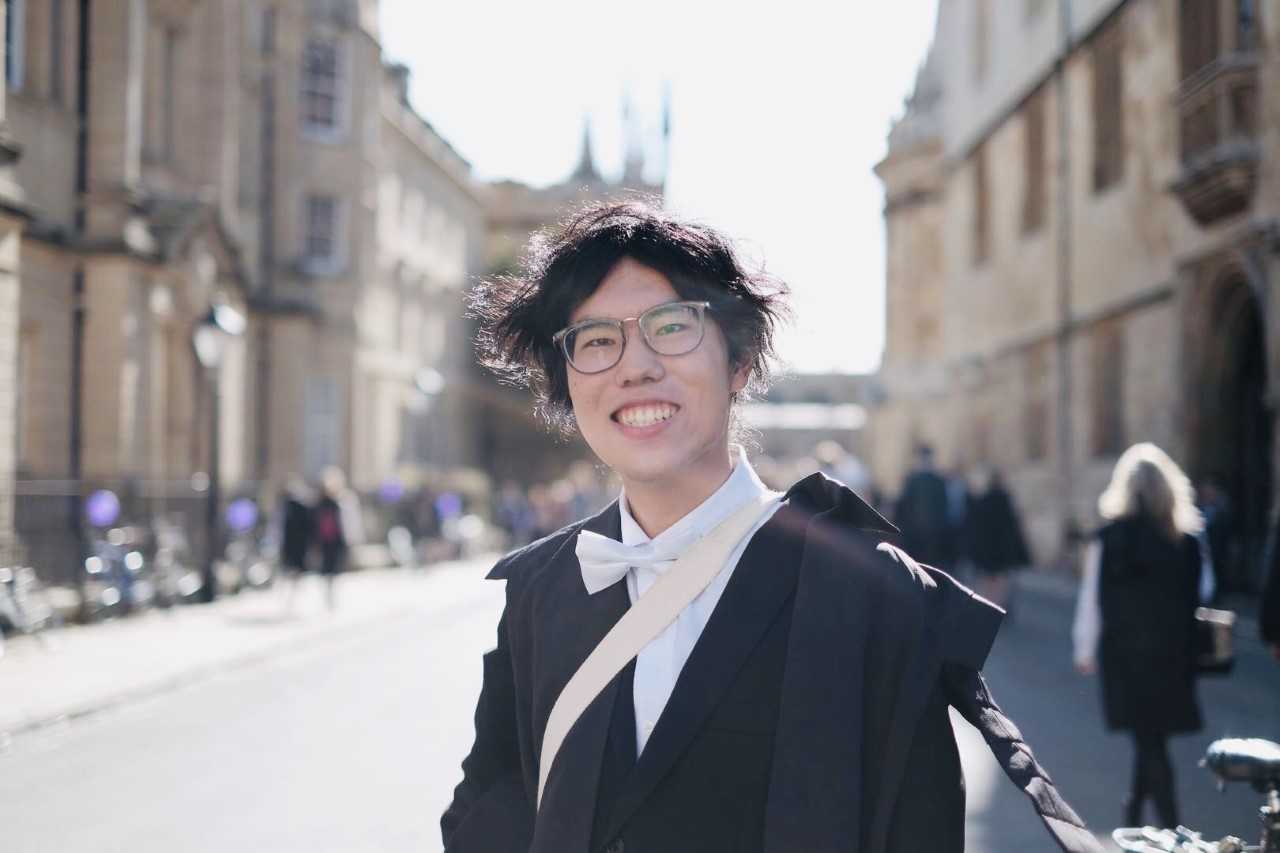 Guoxi in traditional Oxford robes posing in front of historic buildings.