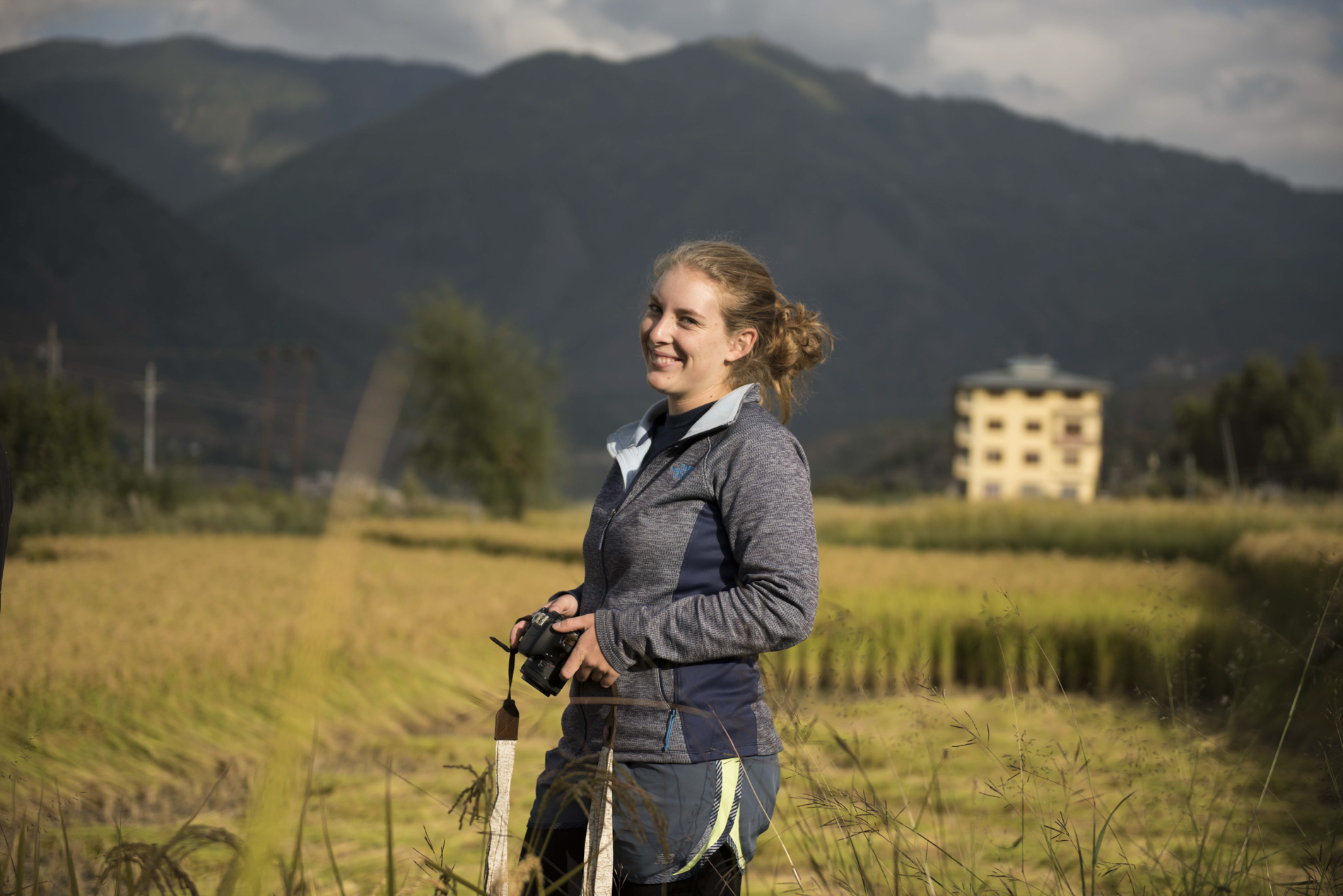 Kinsey standing with a camera in front of a mountain.