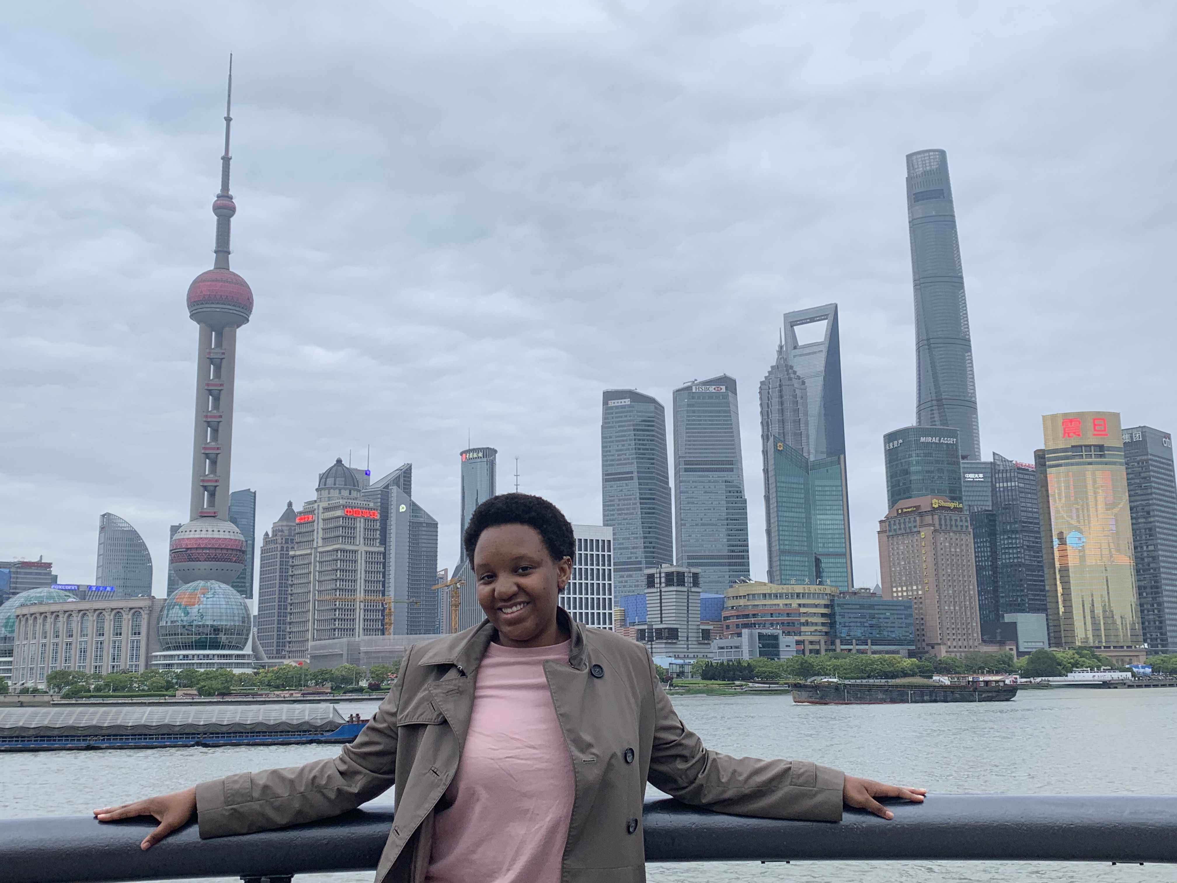 Rolonda standing against a railing in front of the water, with the skyline of Shanghai behind her.