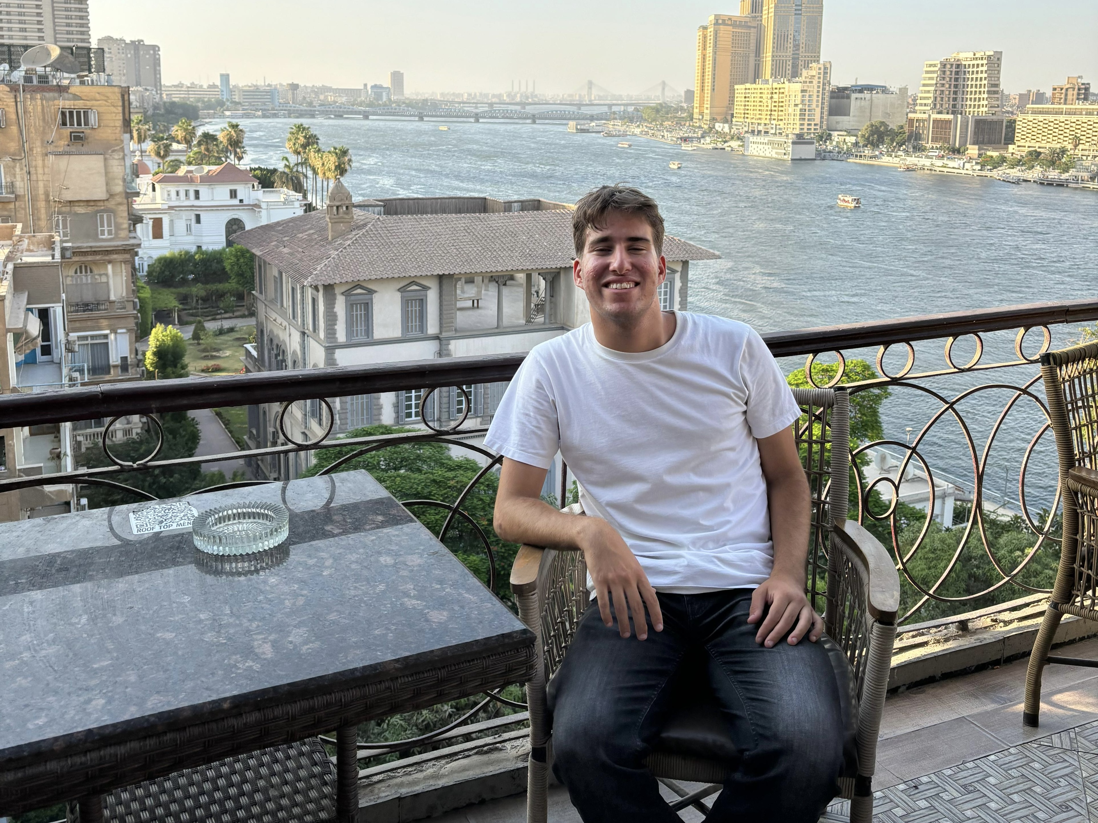 Allan sitting on an apartment balcony in Cairo with a view of the water behind him.