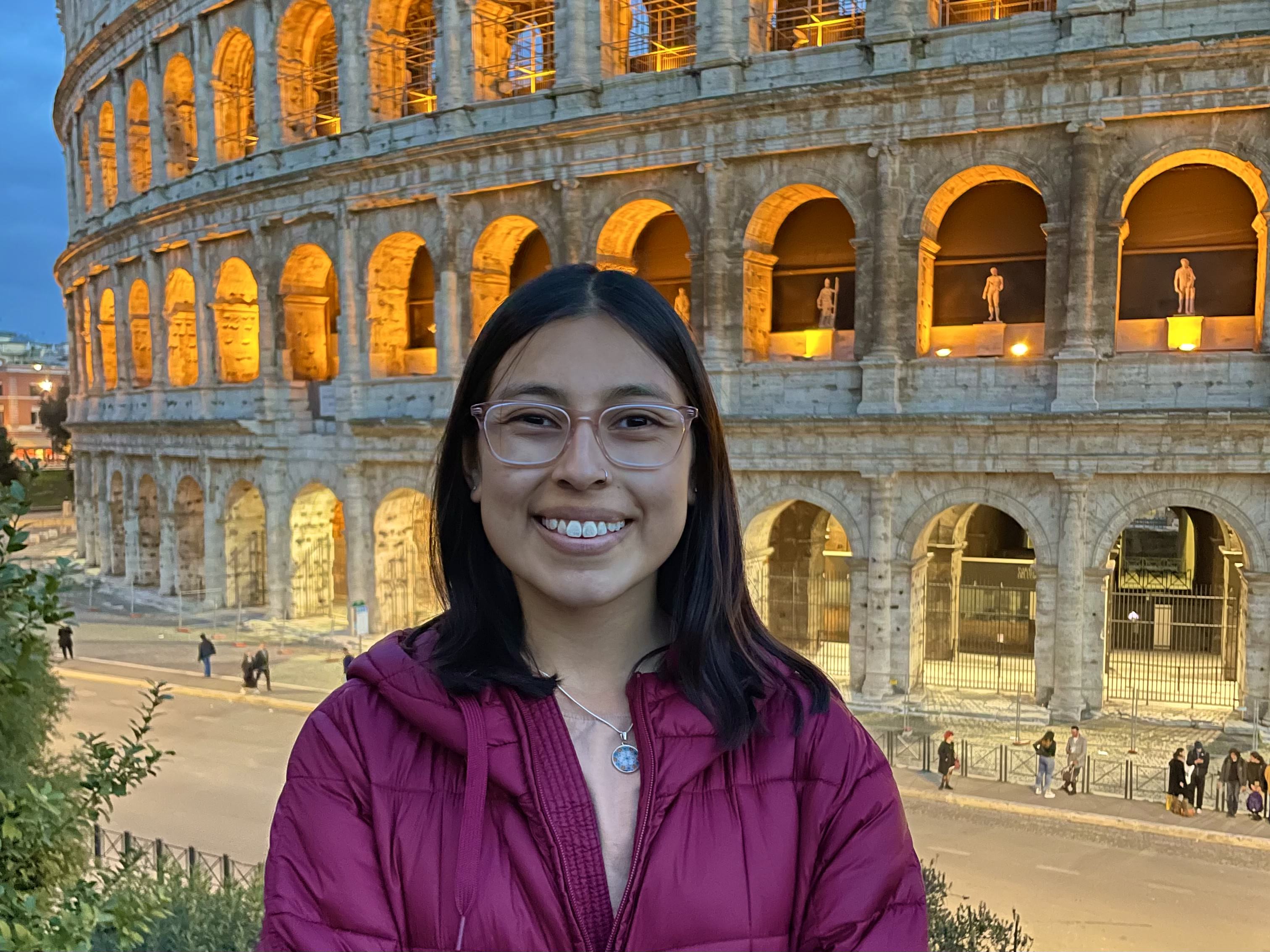 Alex smiling in front of the Roman Colosseum lit up at night.