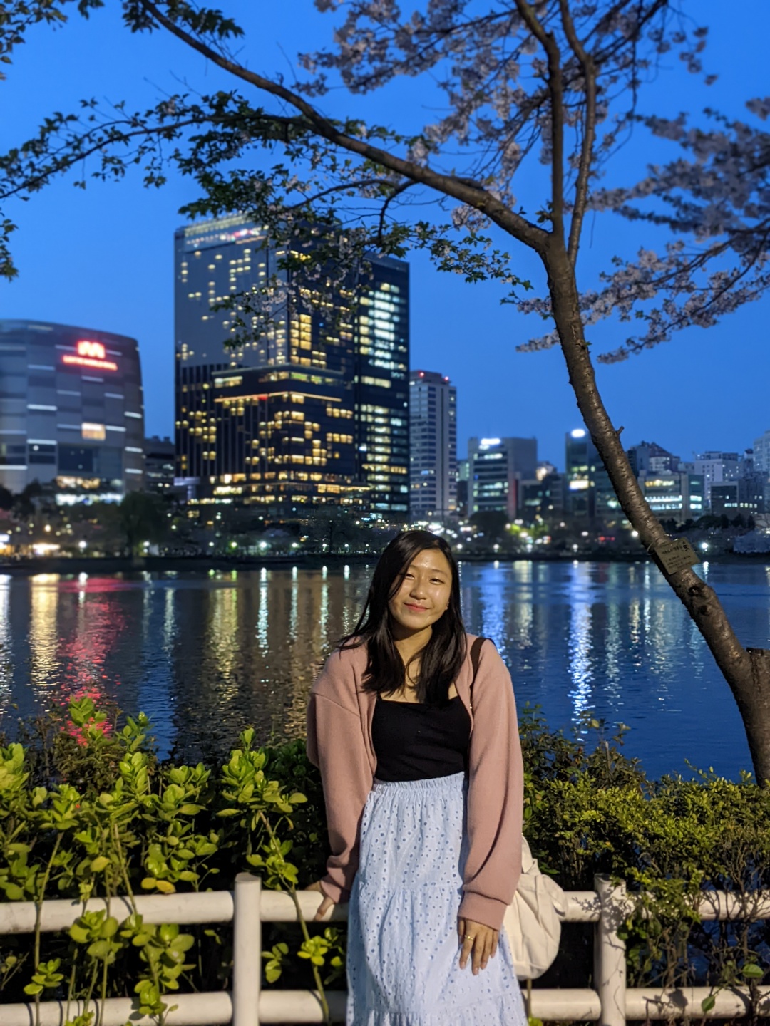Natalie smiling standing in front of Seoul buildings alight at night.