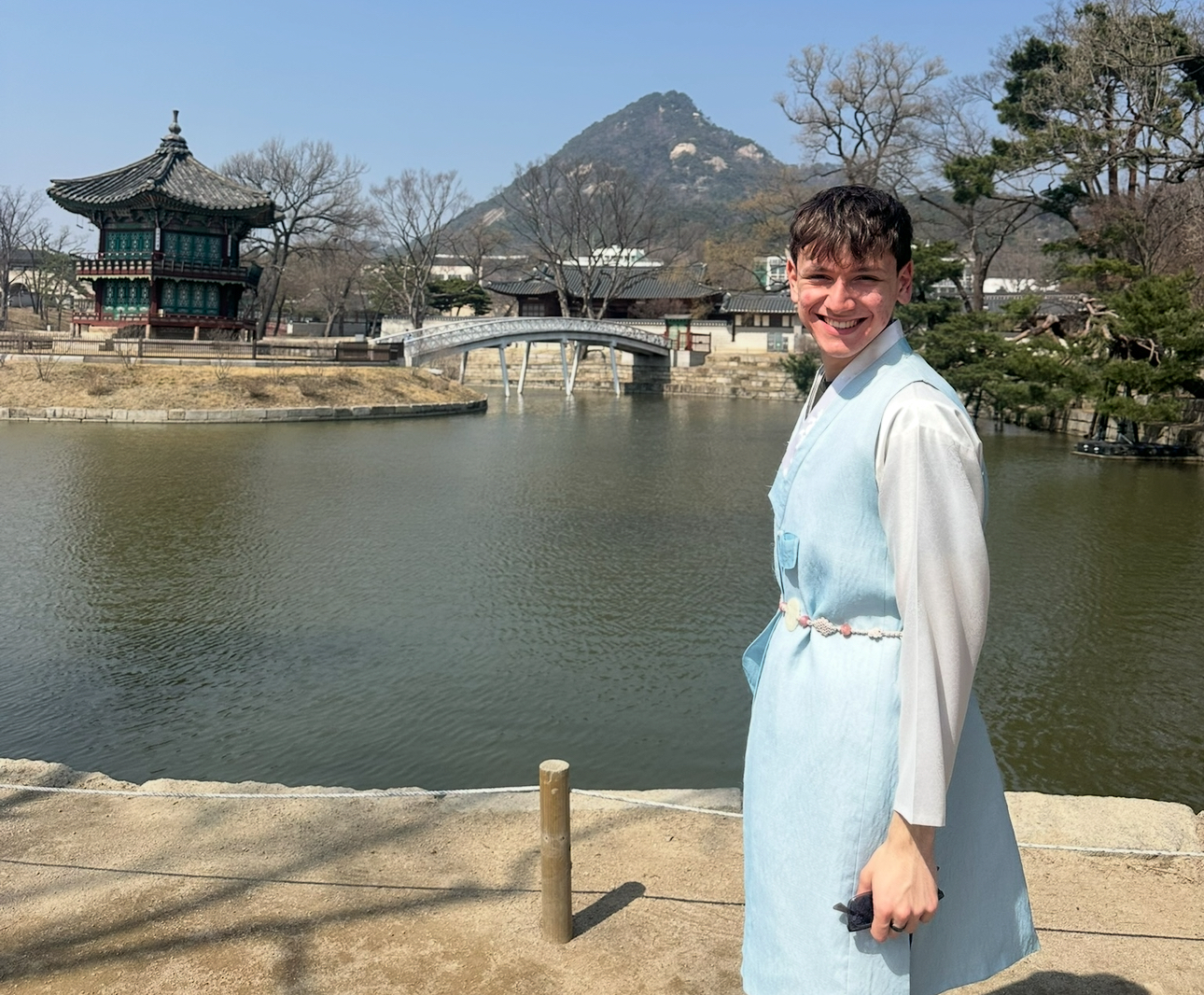 Matthew stands smiling in front of the water with a temple and mountain in the distance.