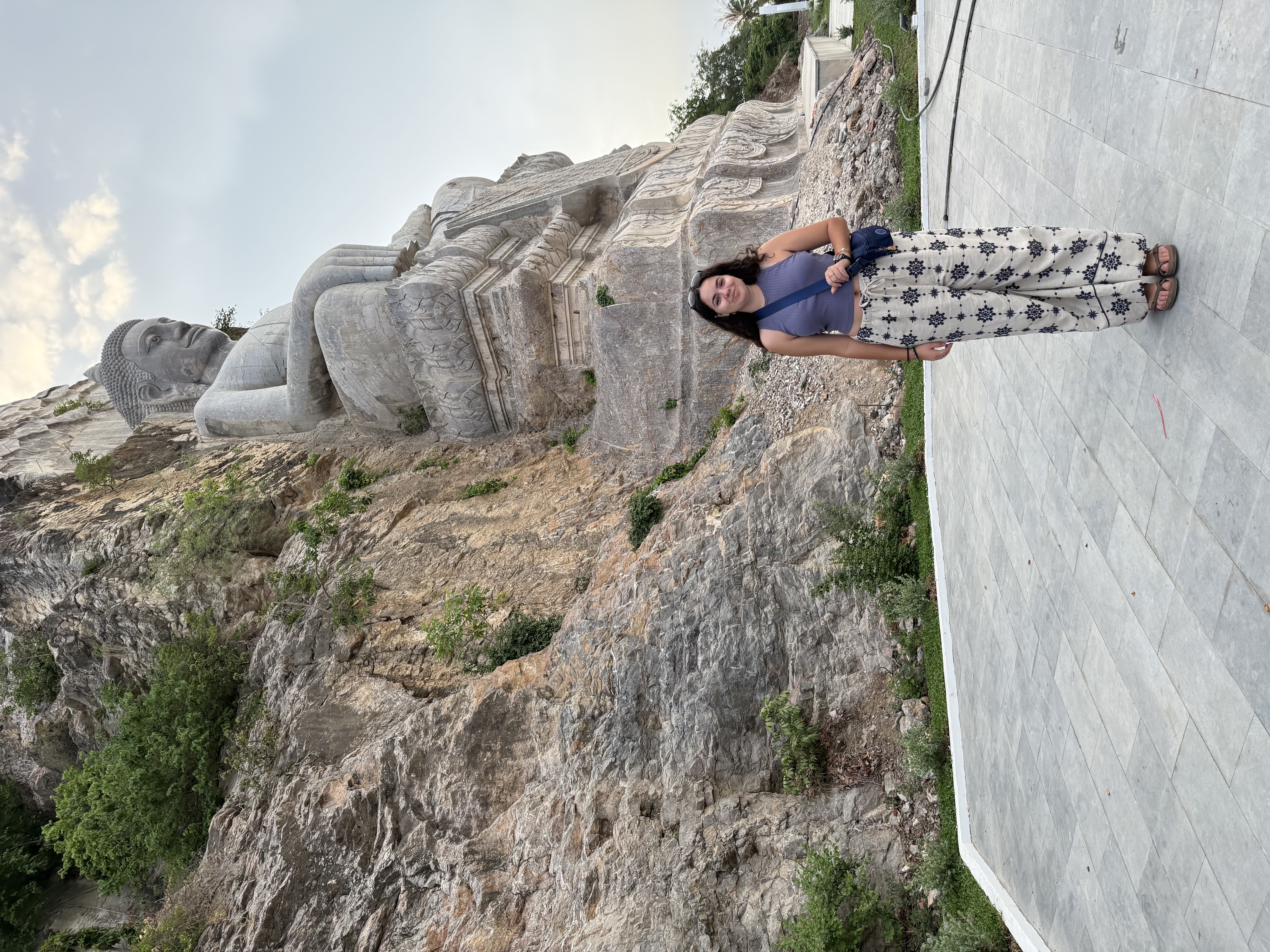 Mia stands in front of a large stone Buddha carved into a cliffside.
