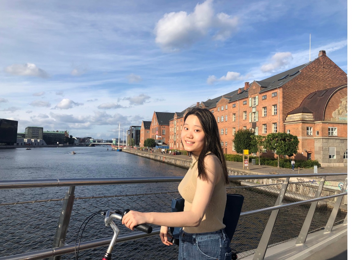 Weini stands smiling beside her bicycle on a bridge in Copenhagen.