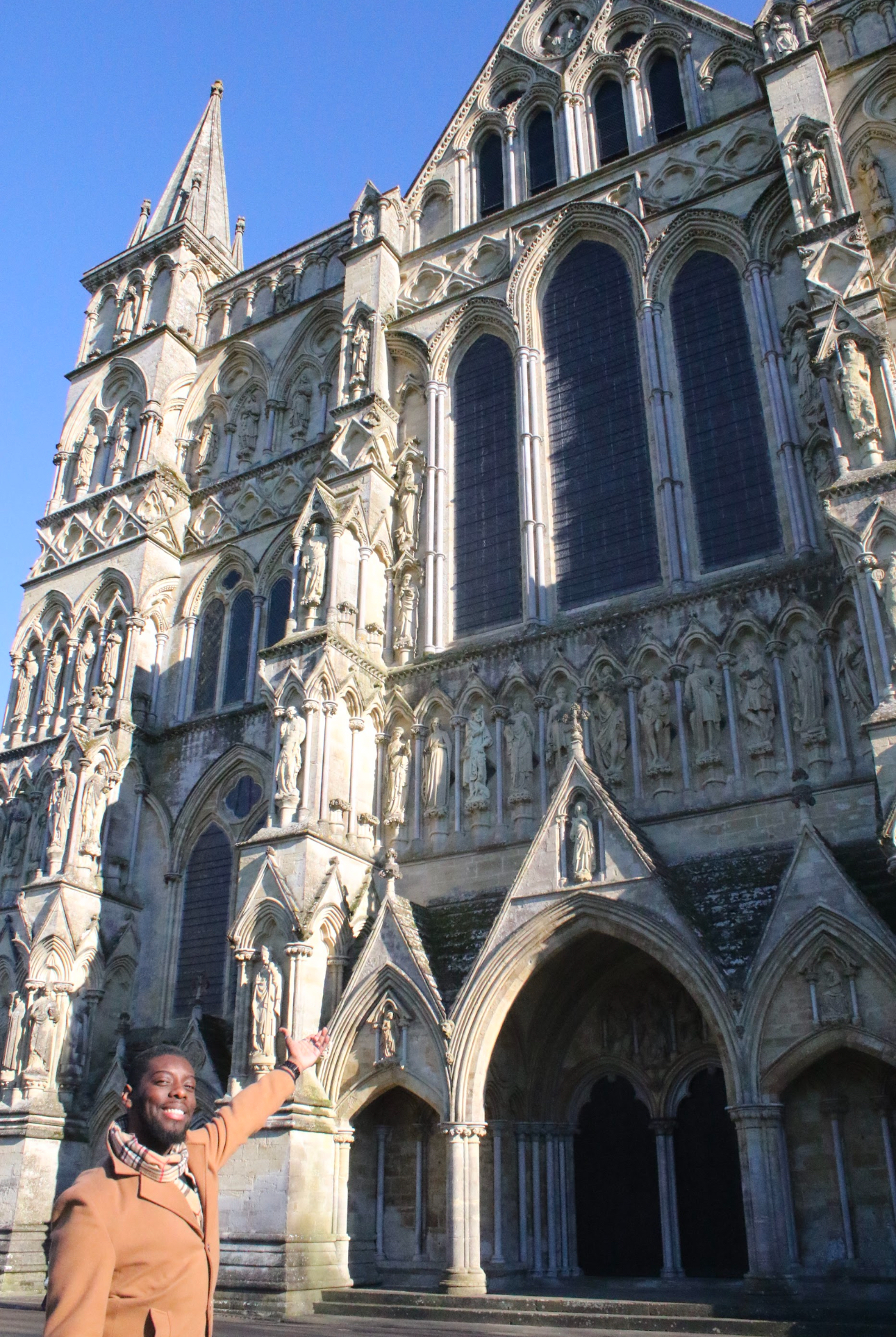 Zaire stands at the base of a cathedral, gesturing up at the intricately carved facade.