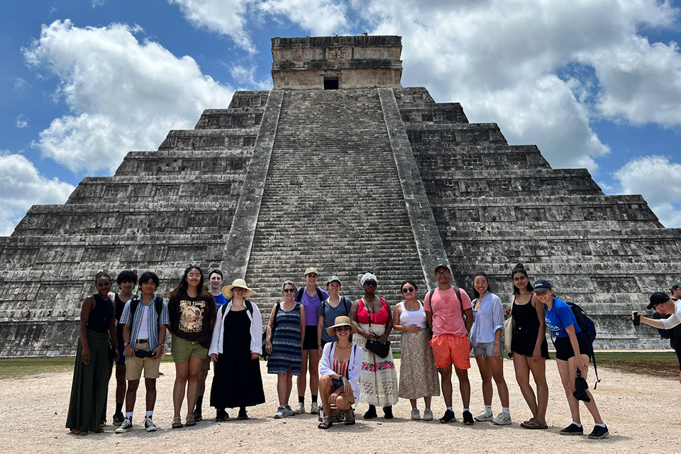 Brandeis students and a Brandeis professor standing in front of a monumental Mayan archeological site at Chichen Itza