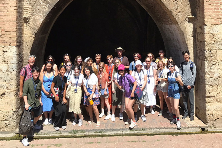 25 students stand with their professor in front of ancient Renaissance architecture