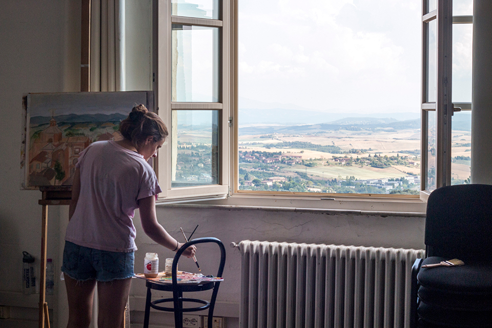 A student painting the Tuscan landscape which she is viewing out the window