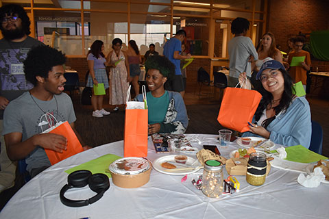 Three students sit at a table smiling and talking.