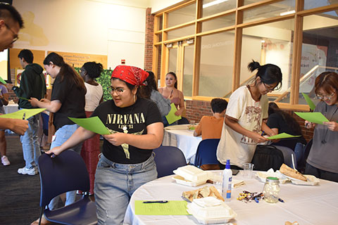 A group of students stand in a room talking to one another.