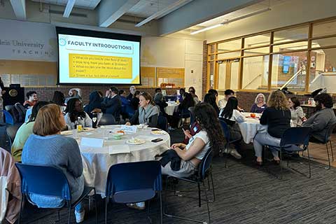 A group of students and professors sit in a room talking.