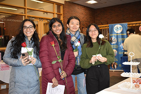A group of four students stand smiling and holding roses.