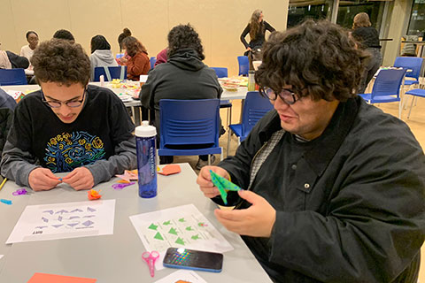 Two students sit at a table crating origami birds.