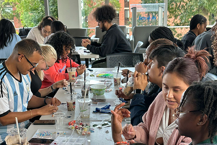 A group of students sit at a table drinking boba tea and making handmade bracelets.