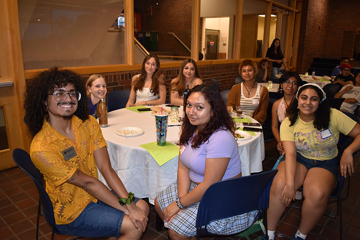 A group of students sit around a table smiling.