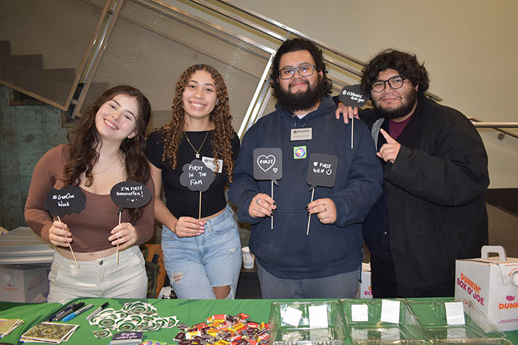 Four students pose with handmade signs with writing about being first generation college students.