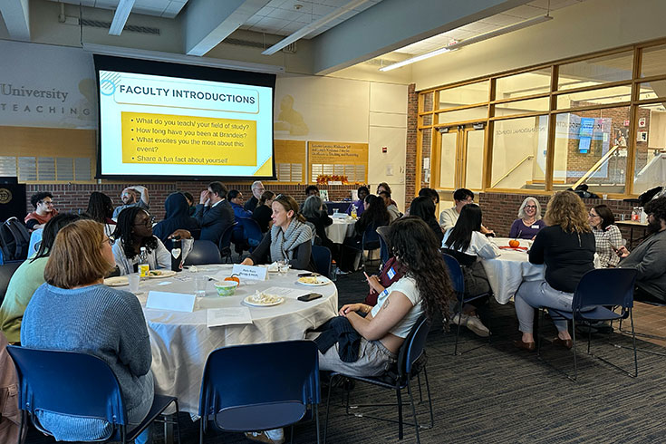 A large group of students and professors sit at tables talking.