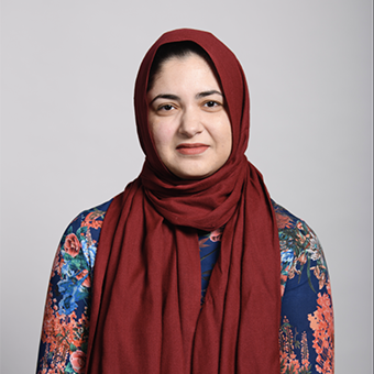 An image of a woman giving a soft smile. She is wearing a muted red head scarf and a floral top.