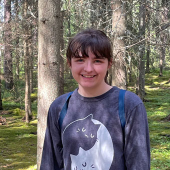 A headshot of Annika. A woman with brown hair and bangs pulled back wearing a shirt with two cats