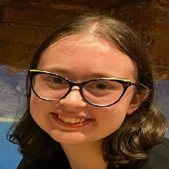 A headshot of Hannah. A woman with brown curly hair. She is wearing glasses and smiling at the camera.