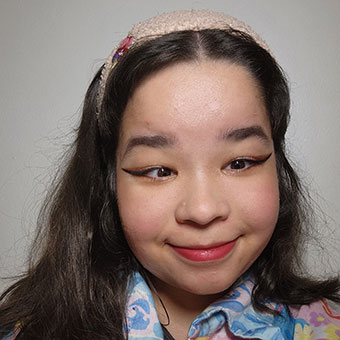 A headshot of Christina. A female with dark hair wearing a pink printed jacket and pink headband.