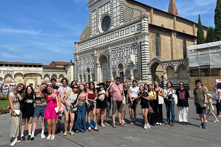 25 students stand with their professor in front of ancient Renaissance architecture