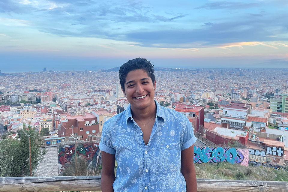 Rani smiles in front of a view of a neighborhood in Spain