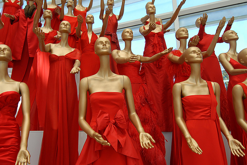 A collection of mannequins wearing various red dresses. The mannequins have their arms raised at various heights.