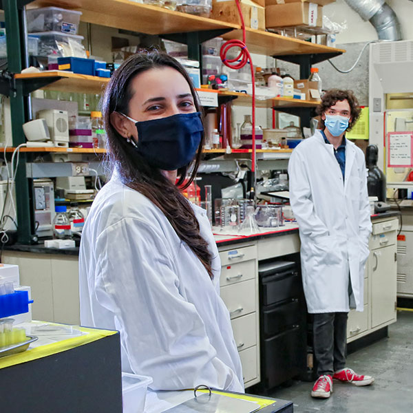 Shoshana stands in a lab while wearing a mask