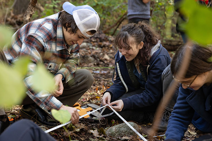 Two students stretch a tape measure to conduct research in the forest