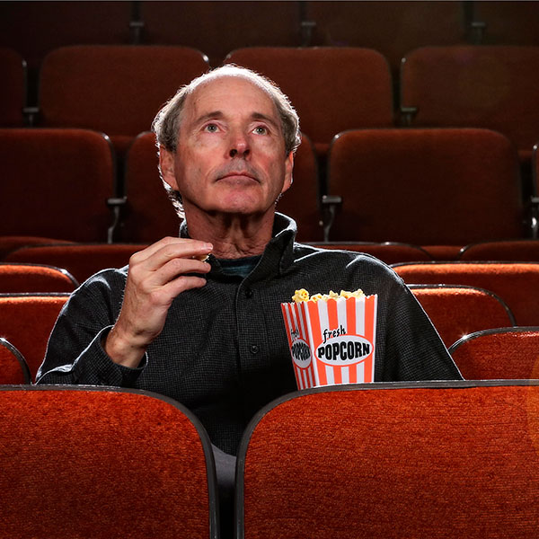 Tom Doherty sits alone in a movie theater eating popcorn