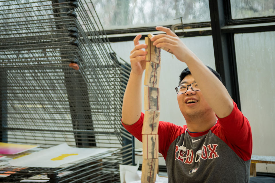 A student in an art studio stacks wooden blocks