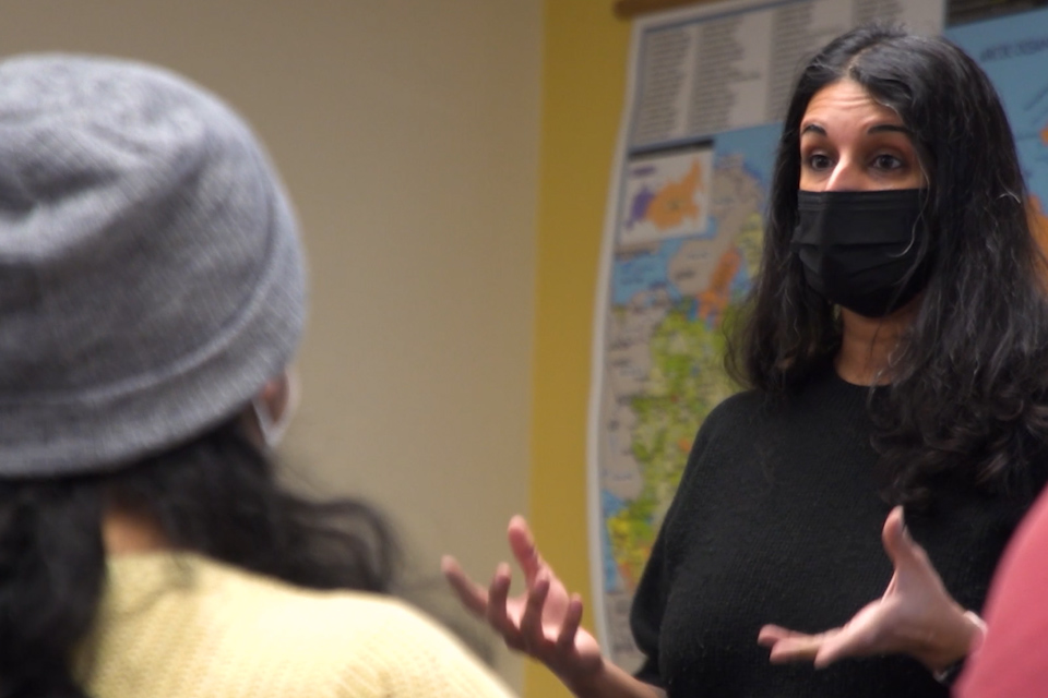 Ulka Anjaria wearing a mask and speaking with a student.