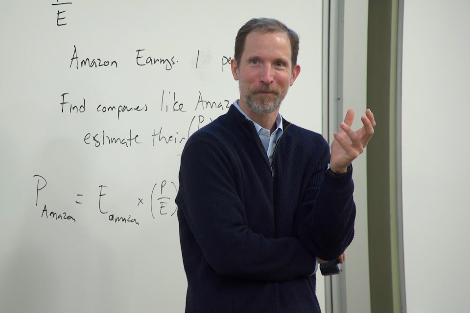 Daniel Bergstresser standing in front of a classroom whiteboard which has text about Amazon company earnings